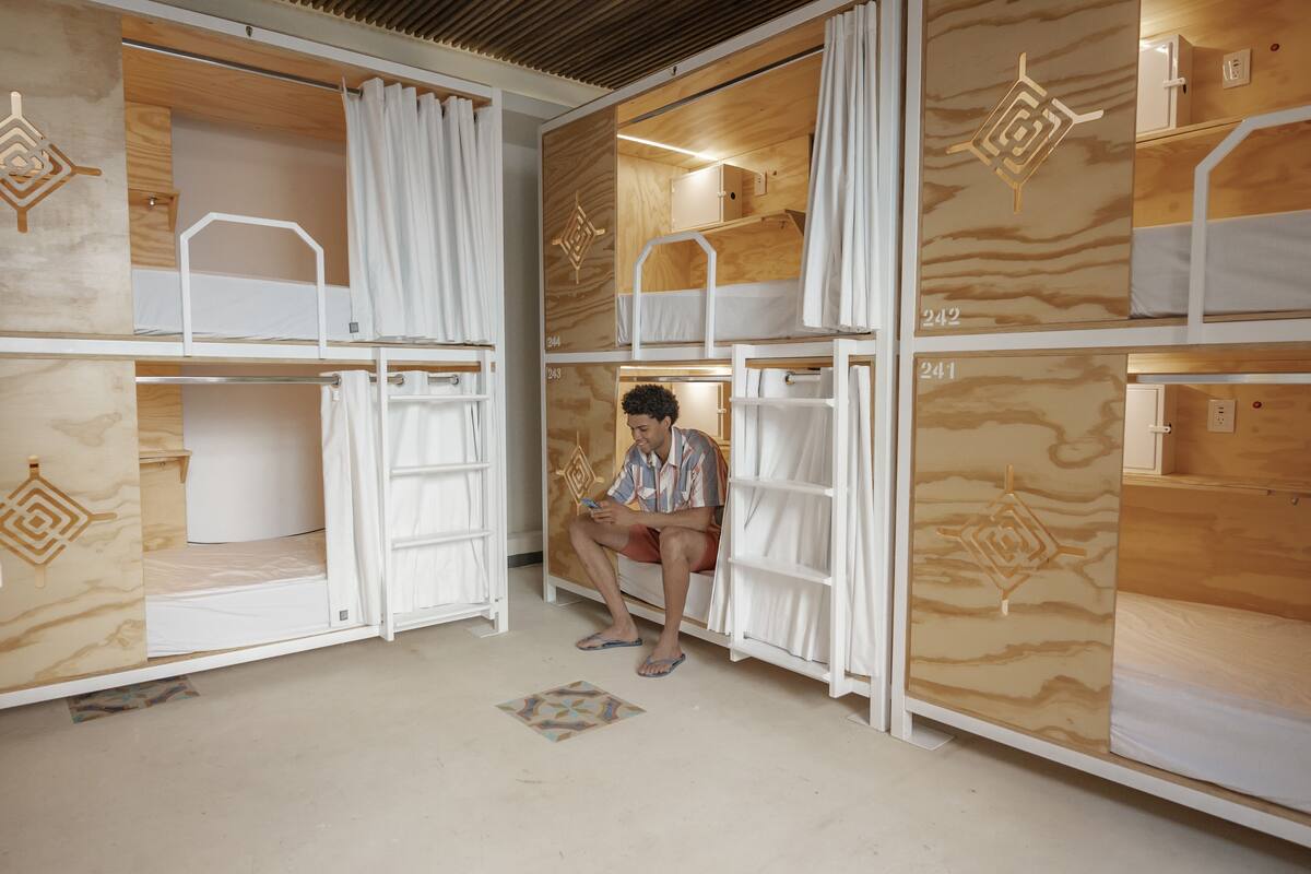 Quarto com beliches, painéis de madeira e uma pessoa sentada na cama.