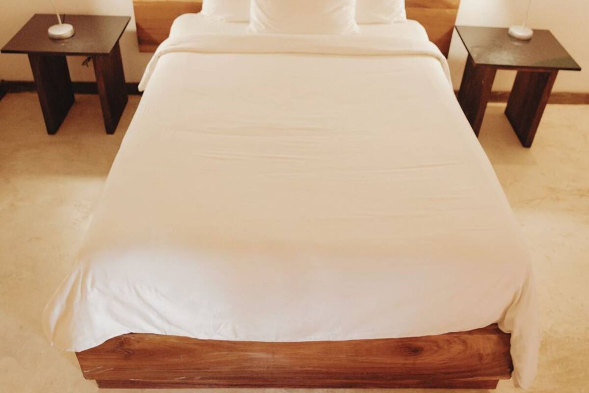 Cama com cabeceira de madeira, roupa de cama branca e duas mesas de cabeceira com abajures.