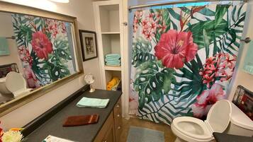 A bathroom with a shower curtain featuring tropical flowers, a toilet, a sink with a mirror, and a towel rack.