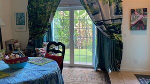 A room with a bed, a chair, a table with a bowl, a rug, and a door leading to a garden.