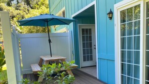 A wooden deck with a table and an umbrella, a door, and a window with a view of the outdoors.