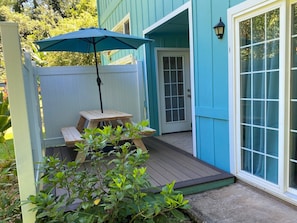 Une terrasse en bois avec une table et un parasol, une porte et une fenêtre donnant sur l’extérieur.