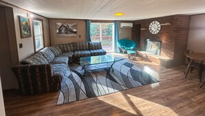 A living room with a sectional sofa, a glass coffee table, a blue chair, a fireplace, and a clock on the wall. - Cozy ORV Cabin Retreat with Firepit & Fast WiFi (West Branch)