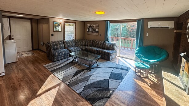 A living room with a sectional sofa, a glass coffee table, and a teal bean bag chair. There is a sliding glass door leading to a deck. - Cozy ORV Cabin Retreat with Firepit & Fast WiFi (West Branch)