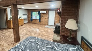 A room with wooden flooring, a bed with patterned bedding, a wooden ceiling, a brick wall, a fireplace, and a TV. - Cozy ORV Cabin Retreat with Firepit & Fast WiFi (West Branch)