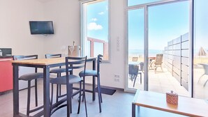 Een moderne kamer met een houten eettafel, zwarte stoelen, een flatscreen televisie en een grote schuifglazen deur die uitkomt op een balkon met buitenmeubilair.