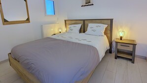 Een net opgemaakt bed met een houten hoofdbord, twee nachtkastjes met lampen en een radiator aan de muur.