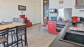 Een moderne keuken met een magnetron, waterkoker en wijnglazen op het aanrecht. Er is een eethoek met een houten tafel en stoelen.