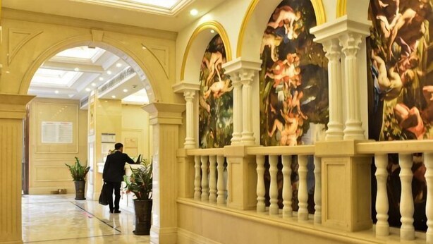 A hallway with a marble floor, classical columns, and a large mural on the wall.