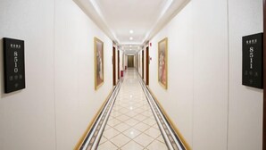 A hotel hallway with a tiled floor, numbered doors, and framed artwork on the walls.
