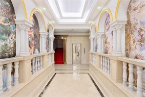 A grand hallway with a marble floor, white columns, and a red carpet leading to a door. - fuyuzhihui Hotel (Wanning)