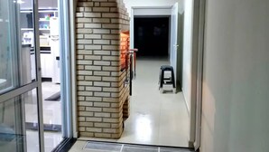 Un corridoio con una parete in mattoni, uno sgabello e una porta che conduce a una stanza buia.