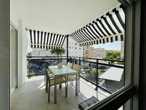 Un balcon avec une table et des chaises en verre, un auvent à rayures et une vue sur le paysage urbain.