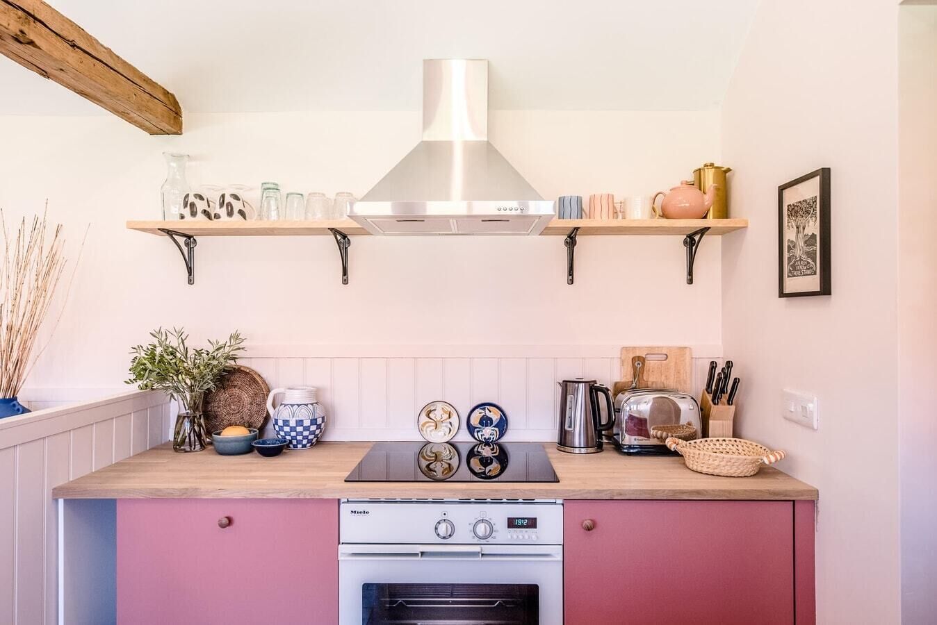 Une cuisine équipée d’une cuisinière moderne, d’une hotte en acier inoxydable et d’un grille-pain. Des étagères au-dessus du plan de travail servent à ranger divers ustensiles de cuisine.