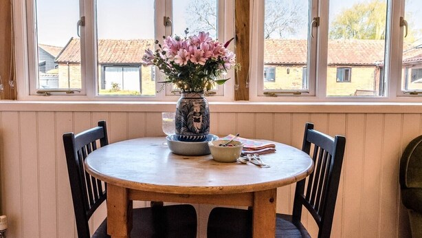 A round wooden table with two chairs, a vase with flowers, and a bowl on the windowsill. - The Studio, Ivy Lodge Barn, Hoo (Hoo)