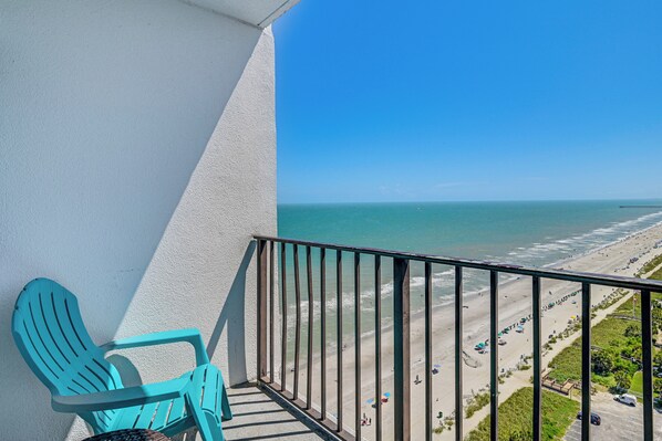A balcony with a turquoise chair, a view of a beach, and a clear blue sky. - Pool Access: Oceanfront Myrtle Beach Getaway! (Myrtle Beach)