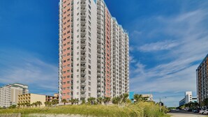 Een hoog hotel met meerdere verdiepingen en balkons, gelegen nabij een strand met palmbomen.