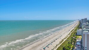 Een strand met een lange zandvlakte, een pier in de verte en gebouwen langs de kust.