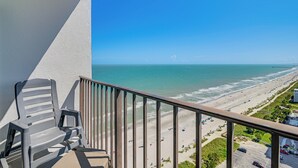 Een balkon met twee stoelen en uitzicht op een strand met mensen en parasols.