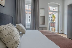 Une chambre avec un grand lit, des rideaux gris, un radiateur et une vue sur un balcon.