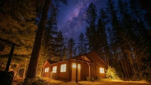 Una cabana amb façana de fusta, envoltada d'alzines altes i un cel nocturn estrellat.