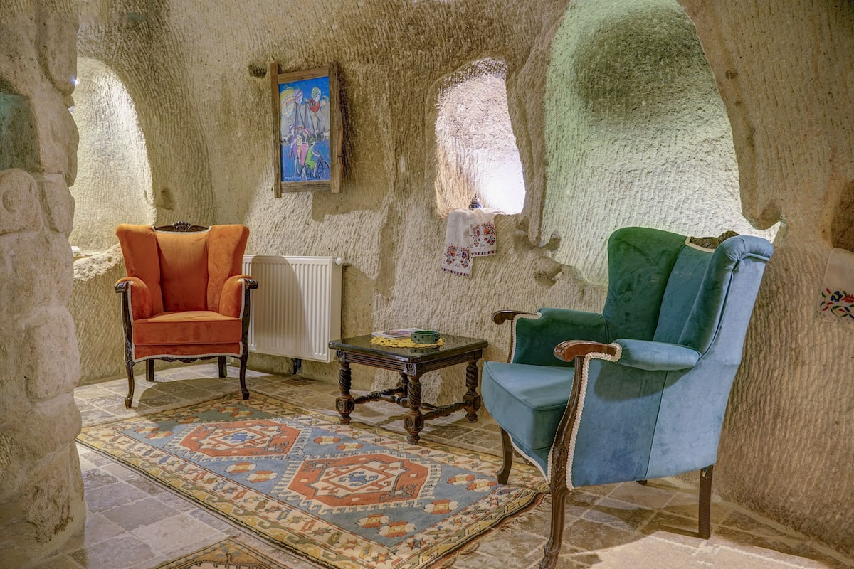A room with a stone wall, two chairs, a small table, and a patterned rug.