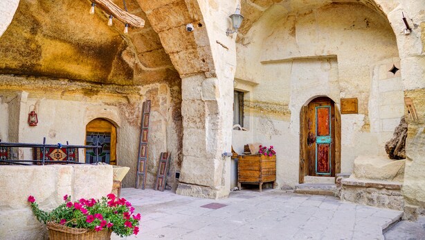 An old stone building with arched doorways, a wooden bench, and a wicker basket of flowers. - Gibos Cave Hotel (Ürgüp)