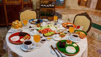 Una mesa de desayuno con diversos platos, entre ellos huevos, tostadas y fruta, sobre un mantel blanco en una habitación de paredes de piedra con una vinoteca al fondo.