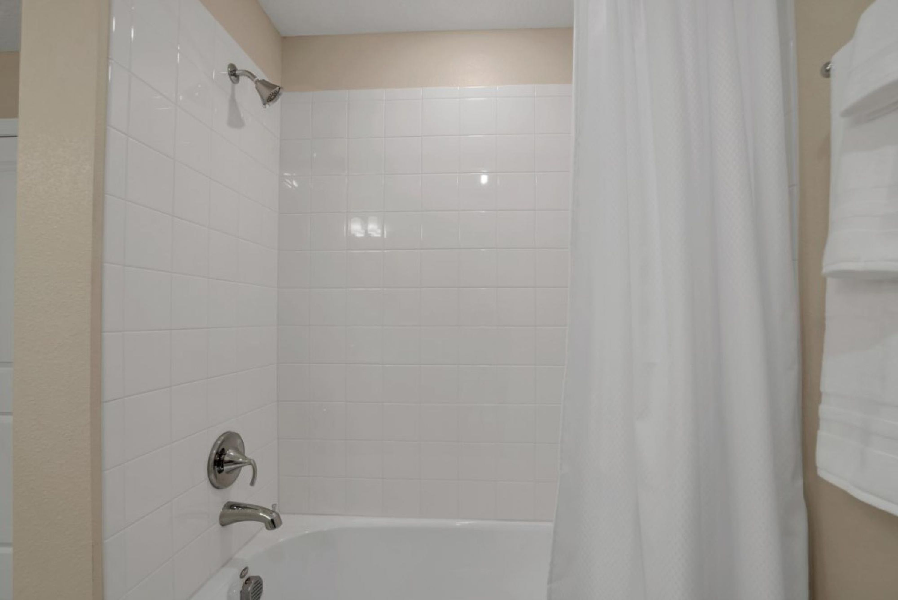 Een badkamer met witte betegelde wanden, een badkuip en een douchekop.