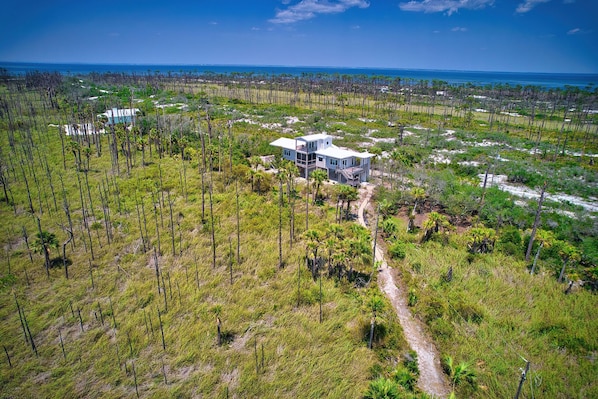 An aerial view of a modern house surrounded by a natural landscape with a clear view of the ocean.