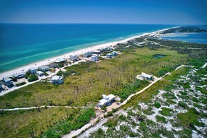 An aerial view of a coastal area with a beach, several buildings, and a forested area.