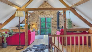 A cozy attic room with a stone wall, a red sofa, a lamp, and a view of greenery outside. - Norton Cottage, Hawkridge (Nr Dulverton)