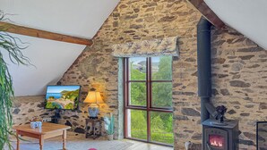 A cozy room with a stone wall, a fireplace, a window with a view, a table with mugs, and a painting. - Norton Cottage, Hawkridge (Nr Dulverton)