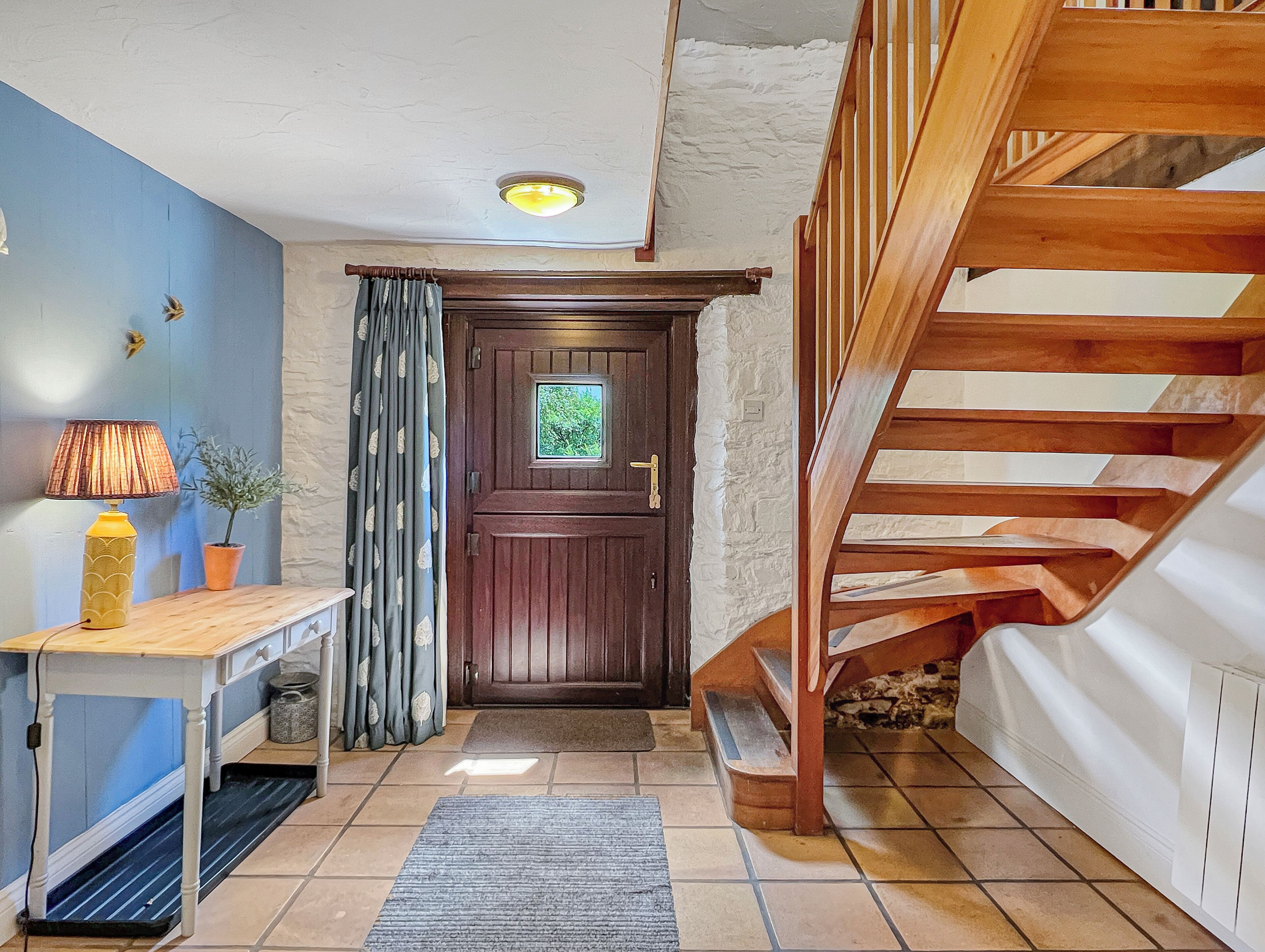 A staircase leading to a landing, a wooden door with a window, a table with a lamp, and a potted plant.