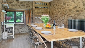 A dining area with a wooden table set for four, a chandelier, and a stone wall. - Norton Cottage, Hawkridge (Nr Dulverton)
