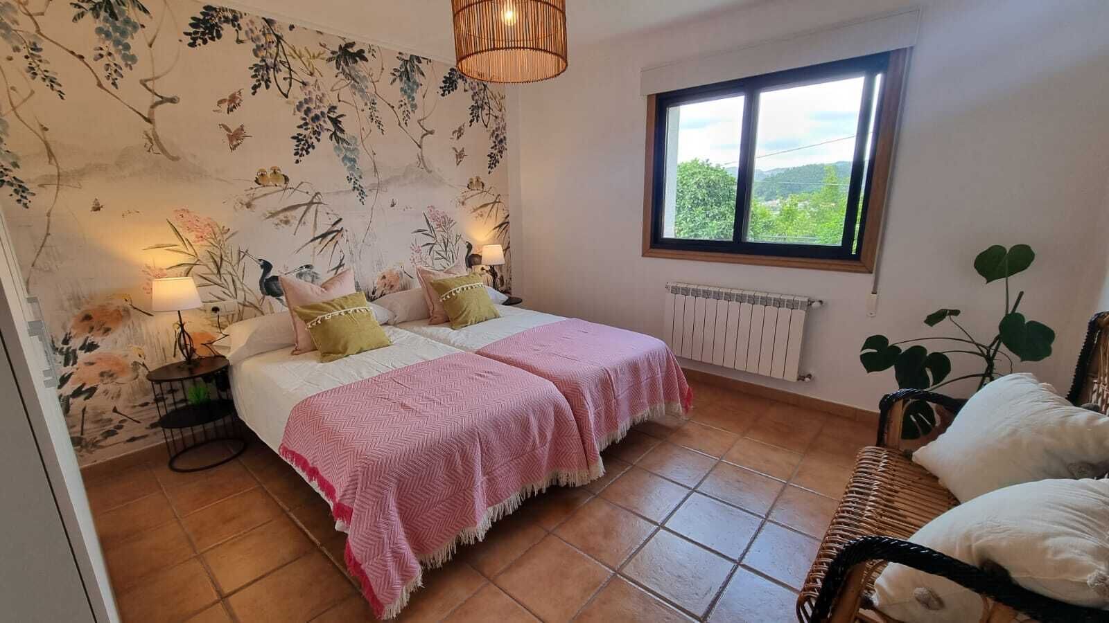 A bedroom with a bed, bedside lamps, a window, a radiator, and a plant.