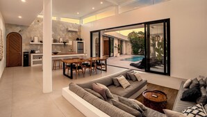 A spacious living area with a large sofa, a dining table, and a kitchen in the background. - Villa Kanina by Alfred in Bali (Pecatu)