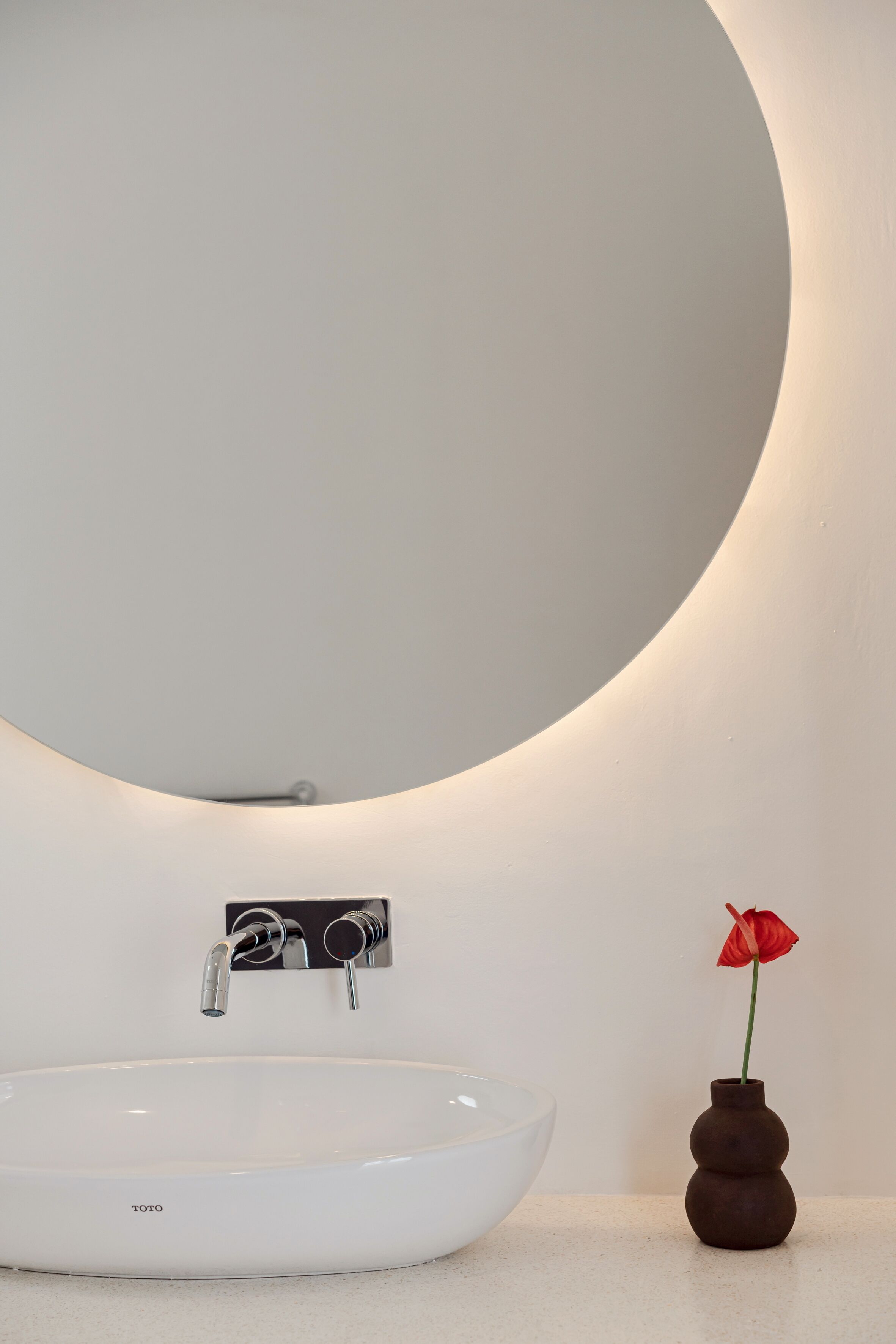 A bathroom with a white sink, a mirror, and a vase with a red flower.