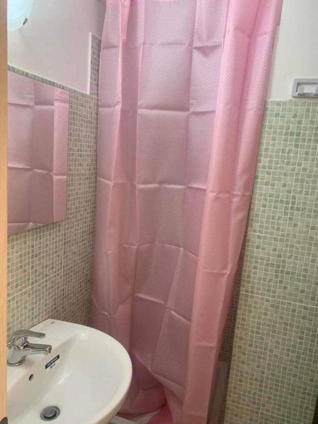 Un baño con lavamanos blanco, un espejo y cortina de ducha rosa.