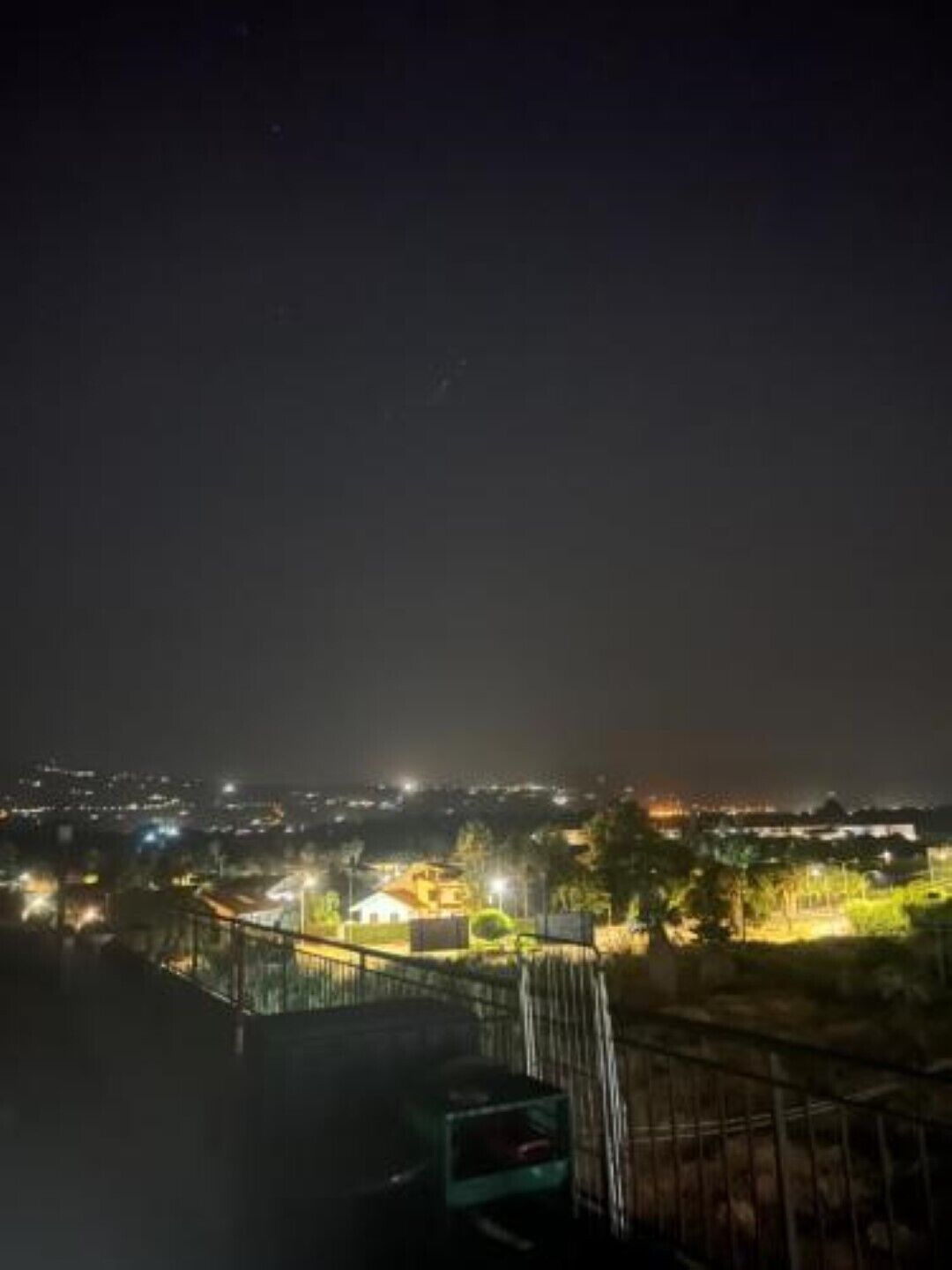 Nachts beleuchtete Stadtansicht mit Gebäuden und einer entfernten Hügelkette.