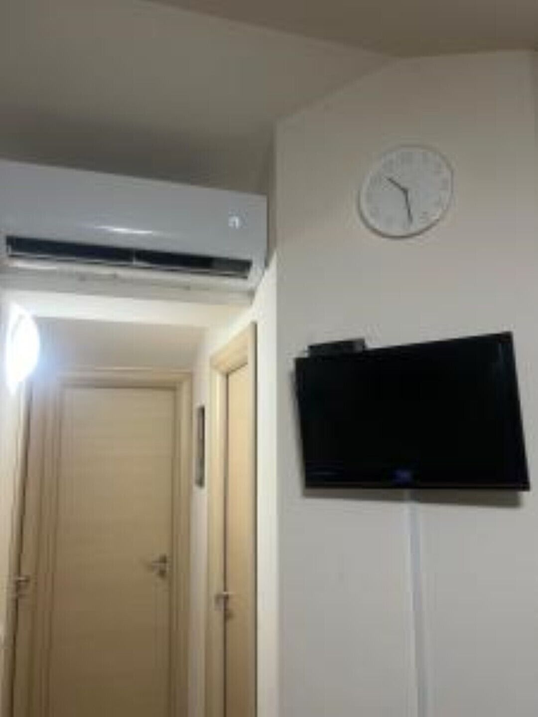 A room with a wall-mounted TV, a clock, and an air conditioning unit.