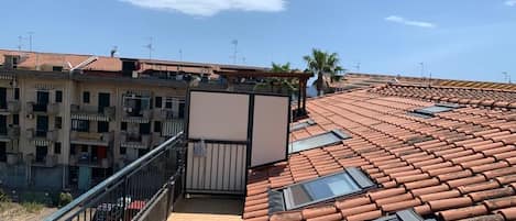 Eine Dachterrasse mit Terrakottafliesen und Oberlichtern mit Blick auf ein Wohngebiet mit Gebäuden und Palmen.