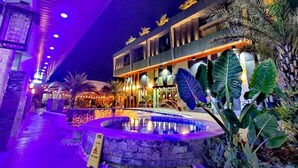 Ein modernes Hotel mit Poolbereich, Außenbeleuchtung und tropischer Bepflanzung.