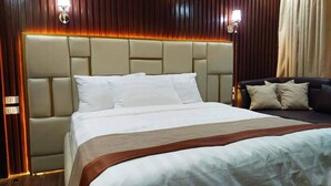 Ein Hotelzimmer mit einem großen Bett, einer Kopfteilbeleuchtung, einem dunkelgrauen Sofa und einer Wand aus Holzpaneelen.