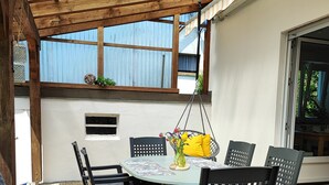 Une terrasse couverte avec une table et des chaises, une plante suspendue et une fenêtre donnant sur un beau paysage.