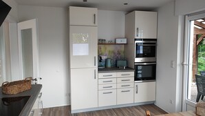 A modern kitchen with white cabinets, a built-in oven, and a dining area with a wooden table.