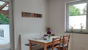 A dining area with a wooden table and chairs, a bench, a window with a view, and a wall-mounted picture frame.