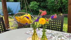 Une table ronde recouverte d’une nappe à motifs floraux, deux vases en verre ornés de fleurs et une lanterne suspendue.