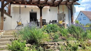Une maison avec un porche en bois, une porte et un petit jardin agrémenté de plantes et de fleurs.
