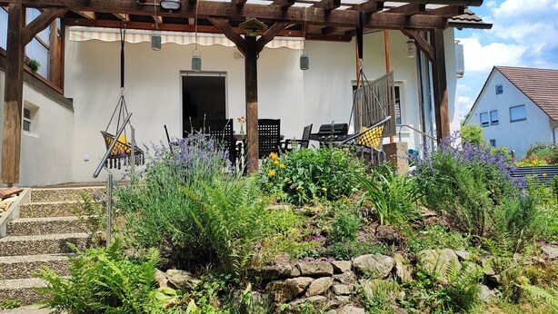 A house with a wooden porch, a door, and a small garden with plants and flowers.